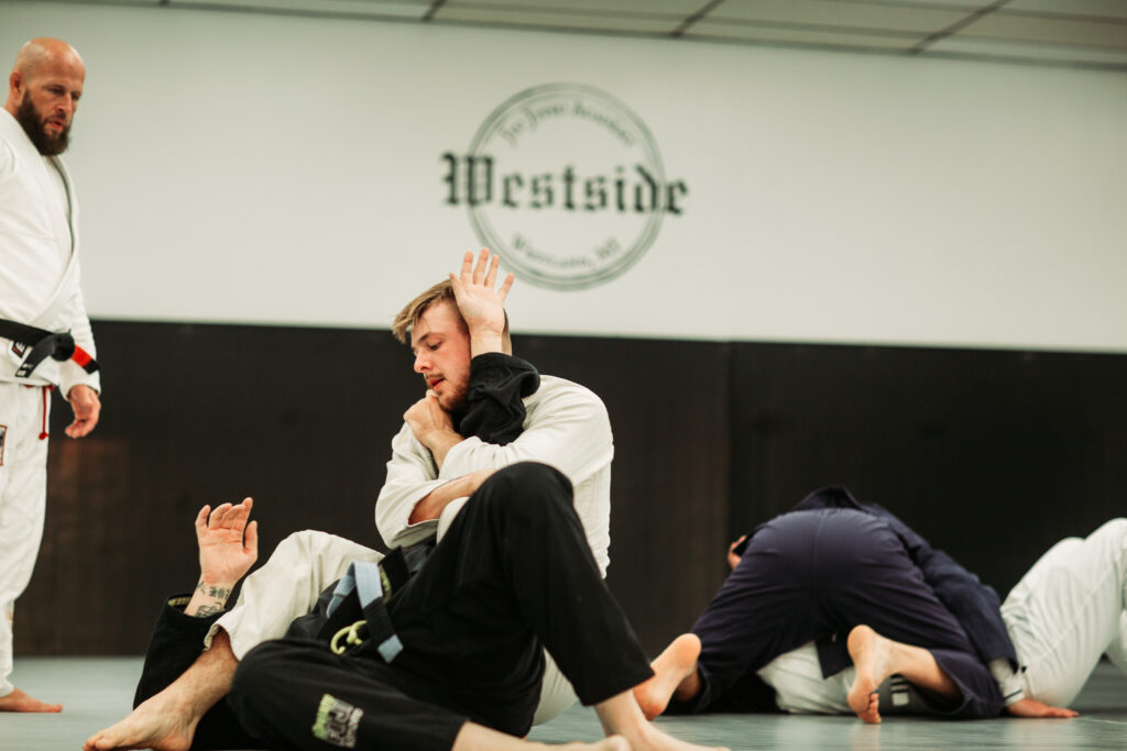 head instructor in white kimono and black belt observing students practicing armbars