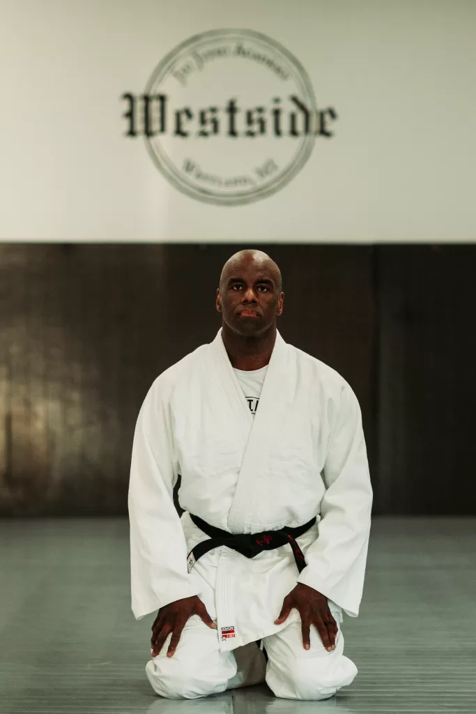 man in white gi and black judo belt kneeling on mat with westside jiu jitsu logo above