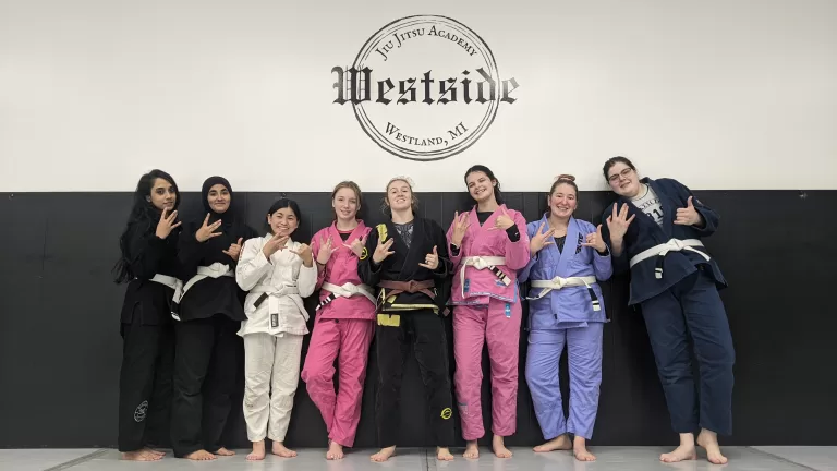 group of women in different colored gi's standing on the wall posing for a photo