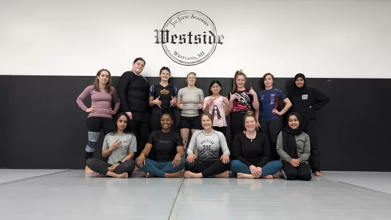 a group of women in 2 rows back row standing front row sitting of different ages, sizes, and ethnicities after womens jiu jitsu class