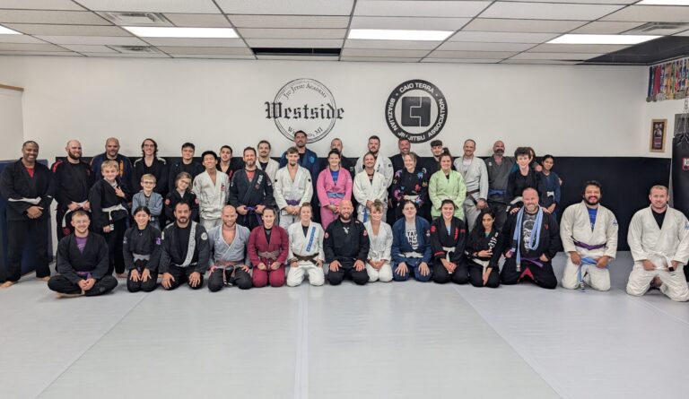 group of people in various colored gi's lined up in rows along the wall, front row kneeling and the middle and back rows standing