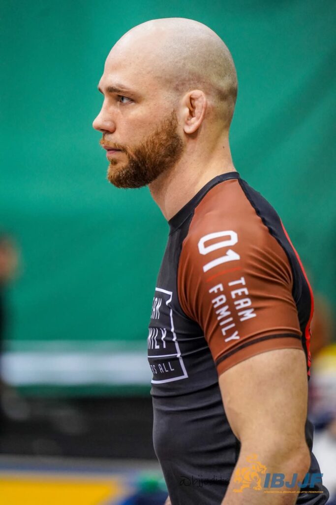 side profile photo of bald man with beard wearing a black and brown compression shirt