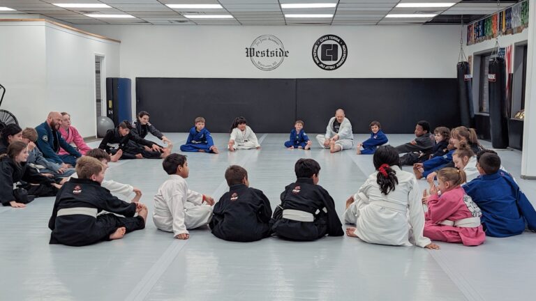 group of children in gi's sitting in a circle doing their after jiu jitsu class stretches