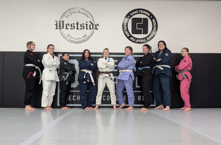 group of women standing along wall mats in gi's with arms crossed