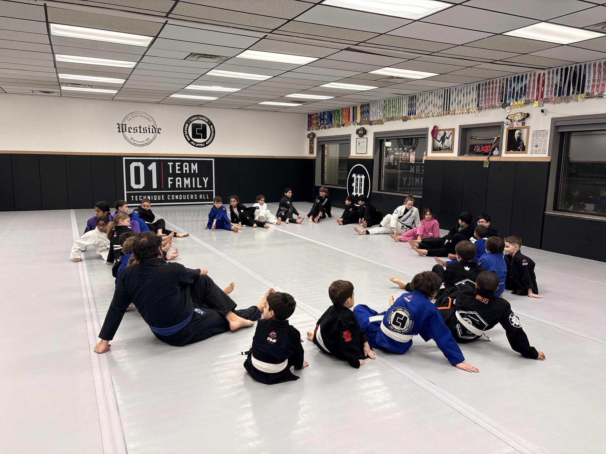 kids wearing jiu jitsu gi's sitting in a big circle on the mat stretching after class